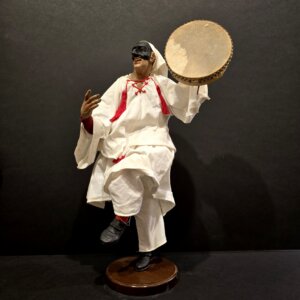 Scultura di Pulcinella artigianale in terracotta, vista laterale con tamburello e abito tradizionale bianco.