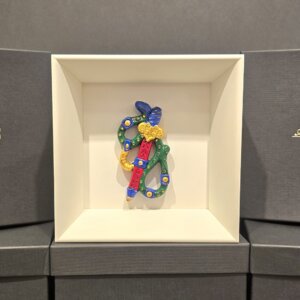 Scultura in ceramica colorata dell’Asso di Spade, decorata a mano con dettagli blu, verdi e dorati, esposta in cornice bianca elegante.