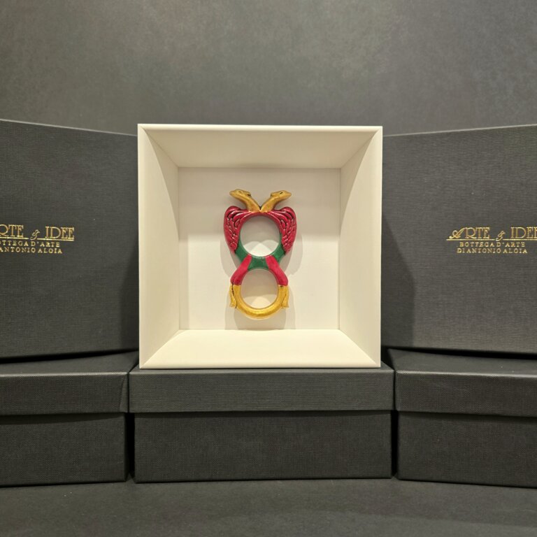 Scultura in ceramica colorata dell’Asso di Denari, realizzata e dipinta a mano, presentata in cornice bianca con sfondo elegante nero.