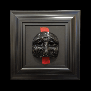 Maschera di Pulcinella nera con cornice nera e pennellata rossa decorativa, simbolo della tradizione napoletana.