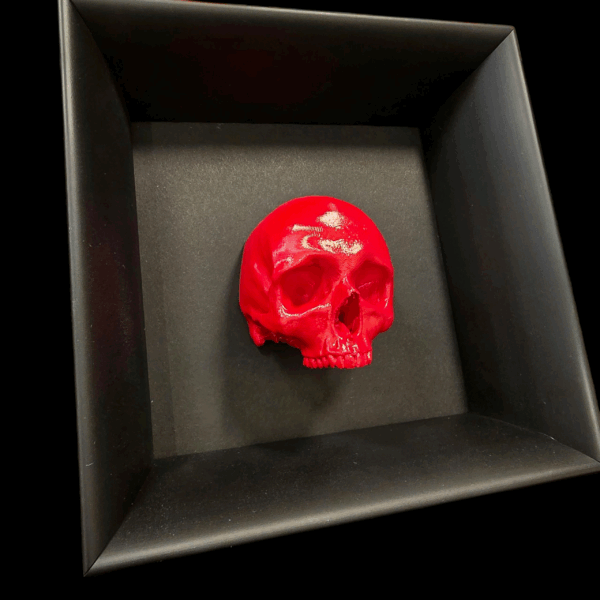 Dettaglio ravvicinato e angolato della scultura a forma di teschio umano con finitura rossa, che evidenzia i riflessi e la tridimensionalità dell'opera.