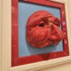 Dettaglio Scultura Ceramica Pulcinella Rosso Primo piano ravvicinato del volto di Pulcinella in ceramica rossa, che mostra i dettagli del naso adunco e delle rughe espressive, in contrasto con lo sfondo celeste.