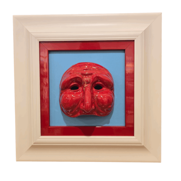 Quadro "Maschera rossa su sfondo azzurro" - Design Pulcinella Quadro quadrato 37x37 cm raffigurante una maschera di Pulcinella in ceramica rossa lucida posta su sfondo azzurro, incorniciata da un bordo rosso e una cornice esterna bianca.
