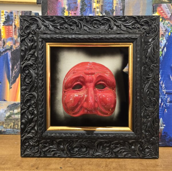 Quadro Maschera Rossa su Specchio Anticato con Cornice Nera uadro quadrato 35x35 cm con cornice barocca nera intagliata, contenente una maschera di Pulcinella in ceramica rossa montata su specchio anticato.