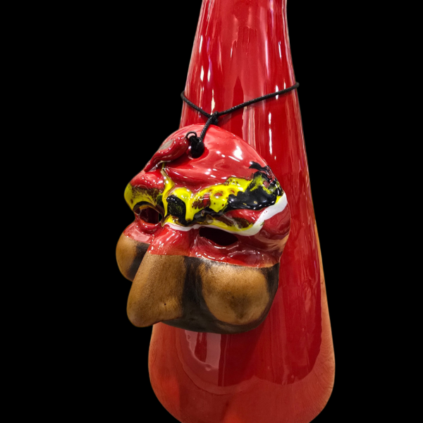 Primo piano della maschera decorativa dipinta a mano in giallo, rosso e nero, legata con un cordino al corno rosso di ceramica.